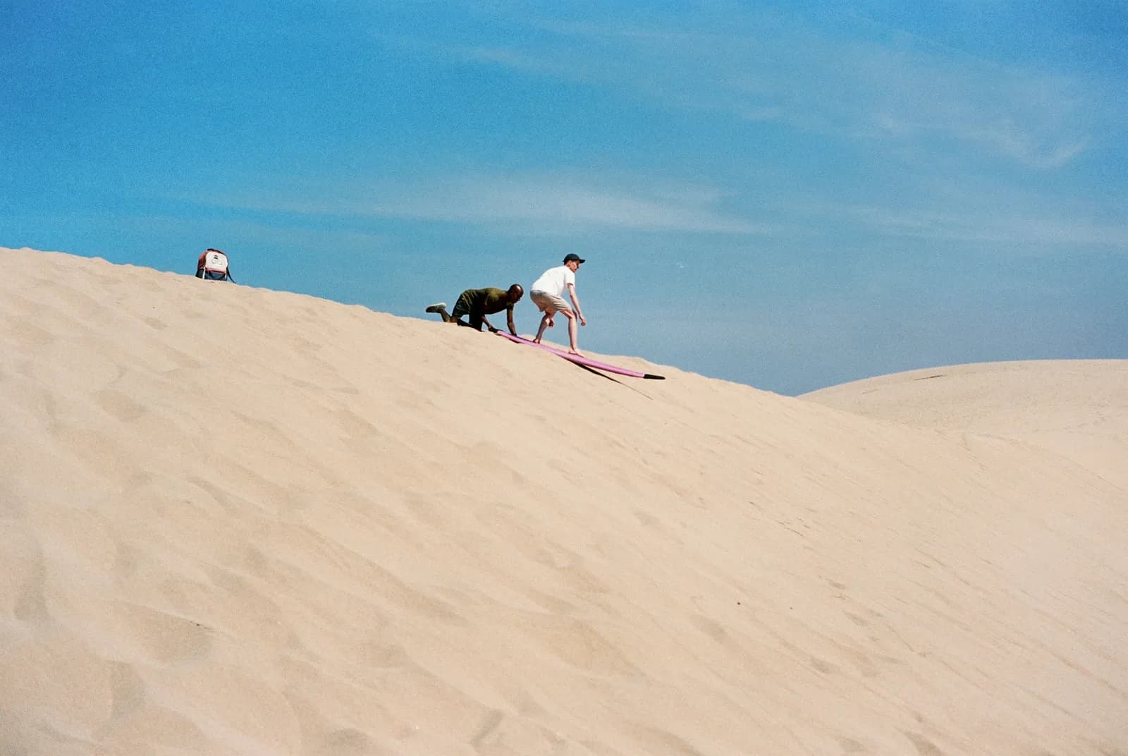 Sandboarding in Essaouira: a rider slides down a large sand dune on a board, steadied by a guide, near Sidi Kaouki — Windy Essaouira